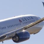 Side closeup of a Delta Air Lines Boeing 737 climbing on takeoff against a blue sky.