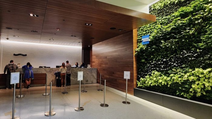 The check-in area at an Amex Centurion Lounge with American Express branding on a wall of greenery on the right side of the counter.