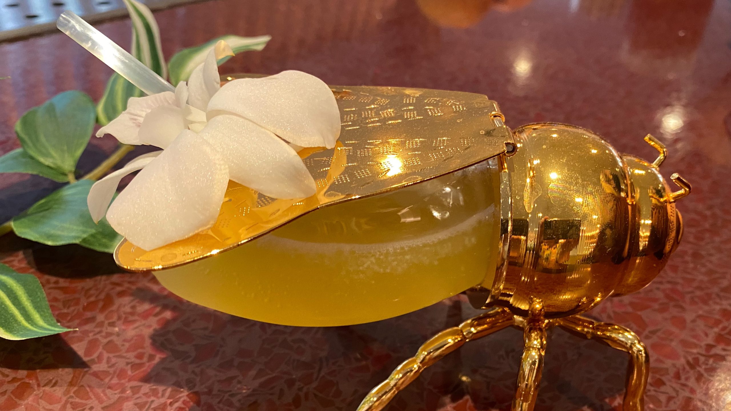 Close-up of a full bee-shaped cocktail glass with a straw and flower garnish.