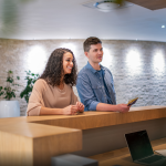 A young couple stand at a hotel front desk speaking to the employee while checking in.