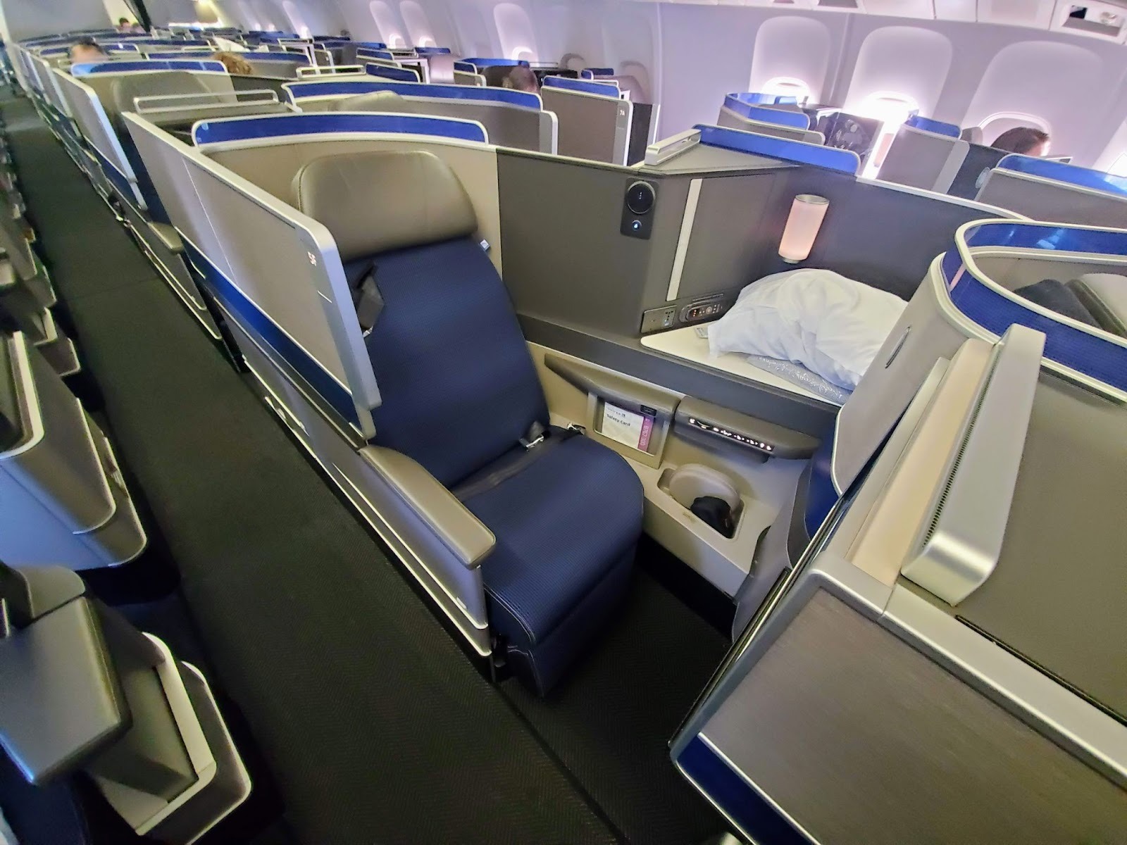 A side view of a United Airlines business class seat showing storage areas, pockets and a cubby with a pillow in it.