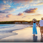 A couple hold hands as they walk near the water on an empty beach during a beautiful sunset.