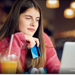 A young woman holds her credit card while shopping online with her laptop.